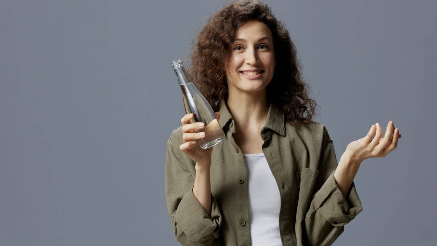 Frau hält ein Glas mit Leitungswasser in der Hand und fragt sich, welche Mythen stimmen.