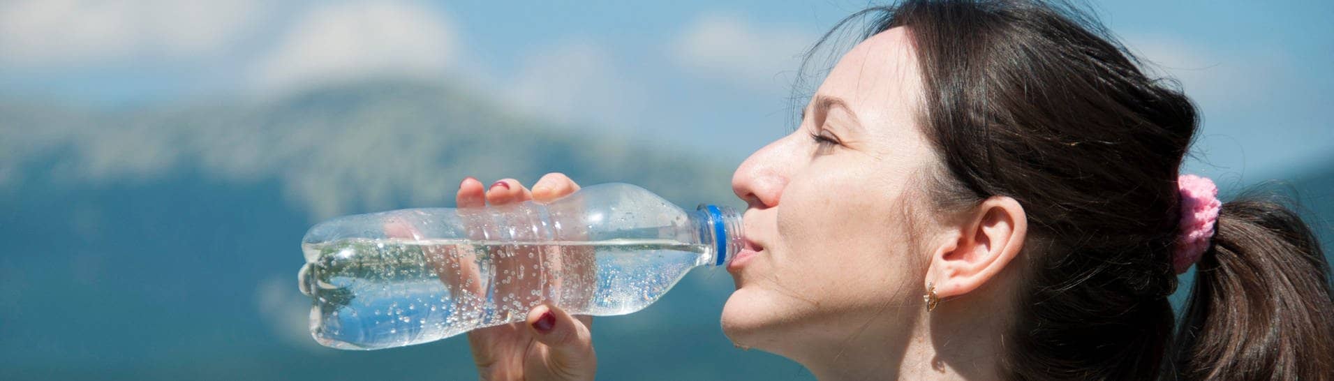 Frau trinkt Wasser vorm Hintergrund der Berge