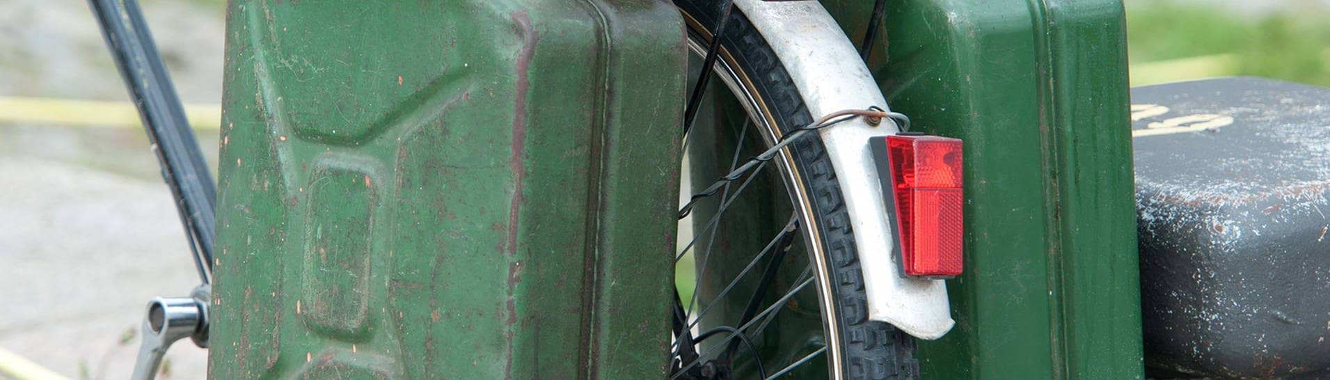 Zwei grüne Benzinkanister, die an einem Fahrradgepäckträger hängen.