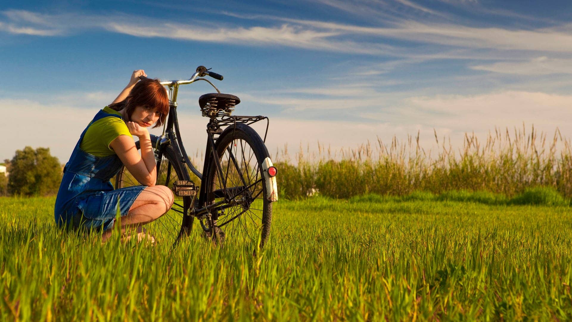 Frau sitzt mit dem Fahrrad in der Wiese an einem sonnigen Tag