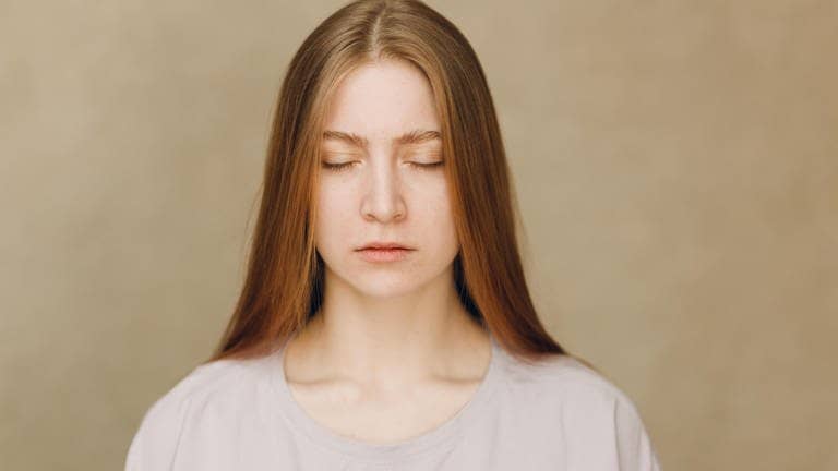Portrait of young sad upset caucasian woman looking at camera against beige background