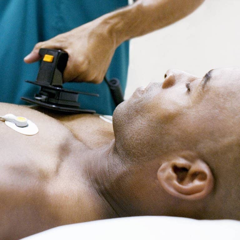 Ein bewusstloser Mann liegt, während ein Mediziner ihm einen Defibrillator auf die Brust hält