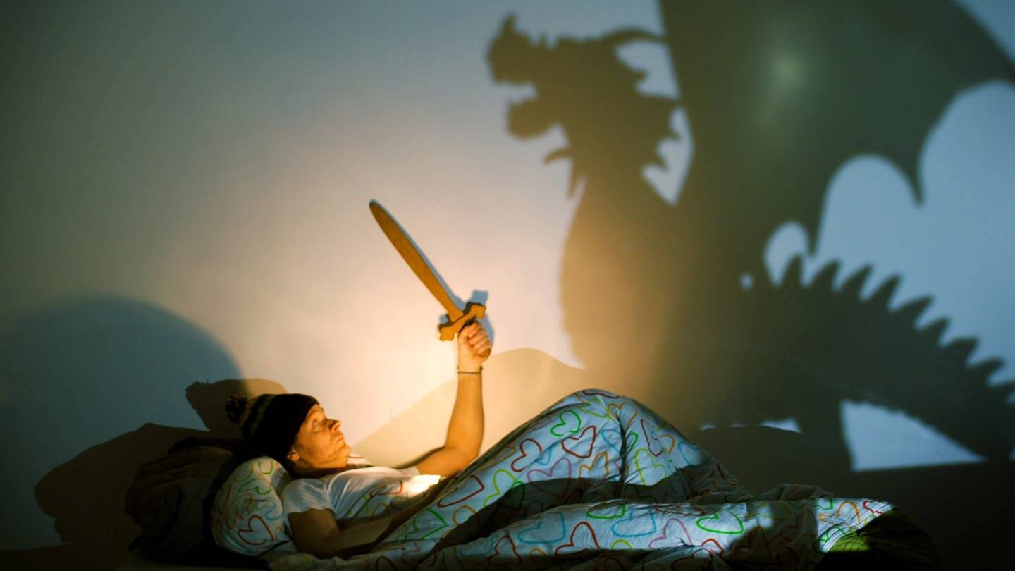 Mann liegt im Bett und kämpft mit einem Schattendrachen