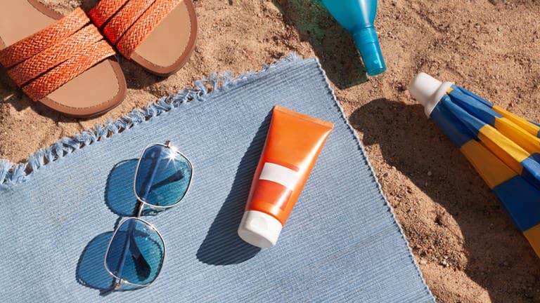 Sonnecremetube liegt auf Strandtuch mit Sonnenbrille und Sonnenschirm (Foto: Adobe Stock, mariarom)