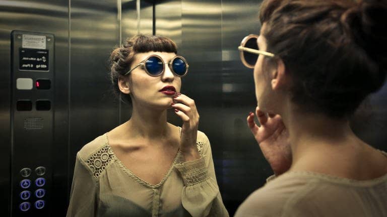 Frau betrachtet sich im Spiegel des Aufzugs (Foto: Adobe Stock, olly)