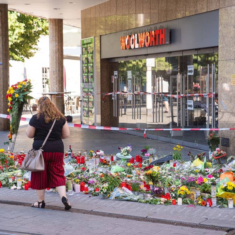 Trauerkerzen und Blumen liegen vor einem Kaufhaus in der Innenstadt, in dem ein Mann Menschen mit einem Messer attackiert hatte. Bei dem Angriff am 25.06.2021 hatte ein Somalier drei Frauen in einem Kaufhaus getötet.