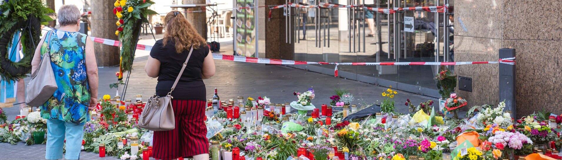 Trauerkerzen und Blumen liegen vor einem Kaufhaus in der Innenstadt, in dem ein Mann Menschen mit einem Messer attackiert hatte. Bei dem Angriff am 25.06.2021 hatte ein Somalier drei Frauen in einem Kaufhaus getötet.