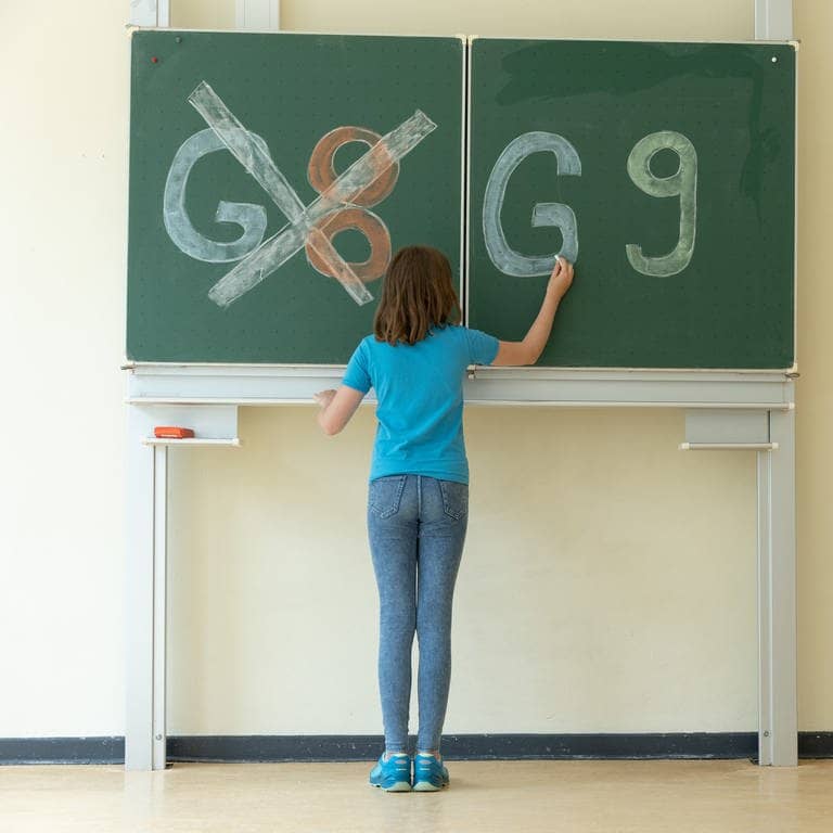 Ein Mädchen schreibt an eine Tafel. G8 ist durchgestrichen, auf der rechten Tafelhälfte steht G9. (Foto: picture-alliance / Reportdienste, Picture Alliance)