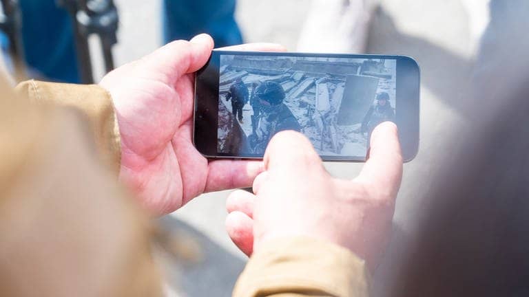 Ein Soldat zeigt auf einem Smartphone ein Video einer Brücke, die von den Ukrainern zerstört wurde, um die russischen Truppen zu stoppen.  (Foto: dpa Bildfunk, picture alliance/dpa | Christophe Gateau)