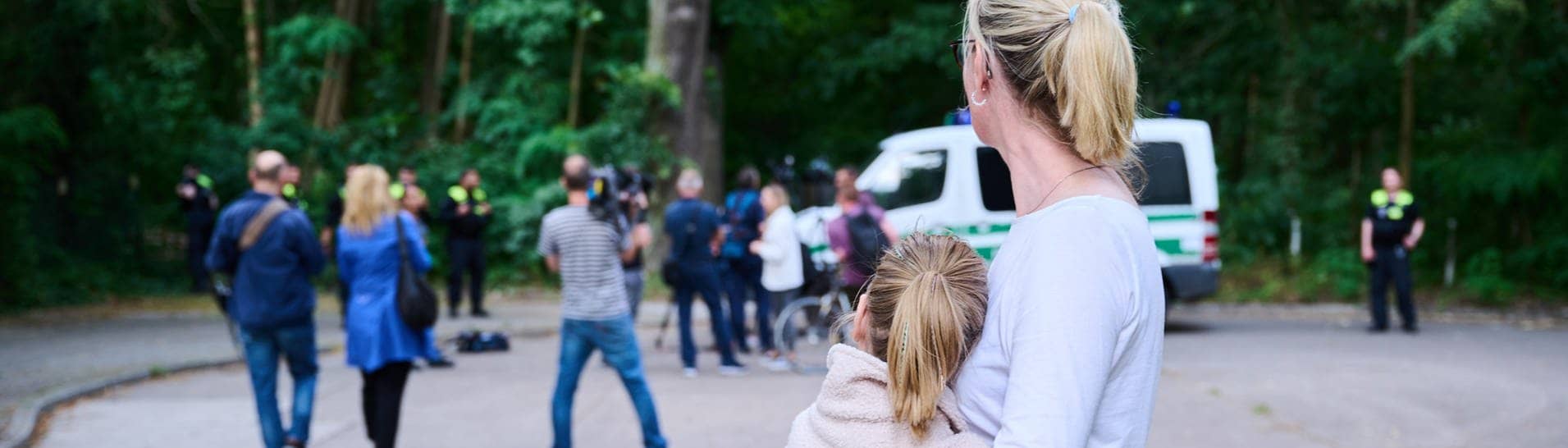 Pflanzenfresser statt Löwin in Berlin: Eine Anwohnerin und ihre Tochter sehen dem Treiben von Journalisten und Polizei zu, während Tierexperten und Polizeibeamten in einem Waldgebiet in Zehlendorf stehen. 