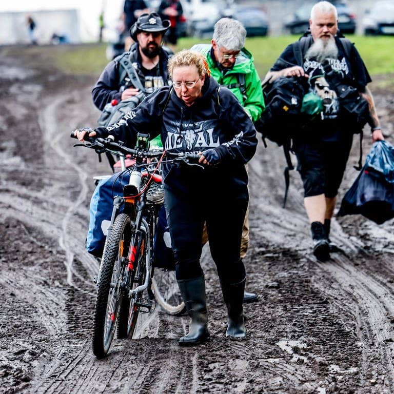 Festivalbesucher verlassen das verschlammte Campinggelände des Wacken Open Air mit ihren Fahrrädern.
