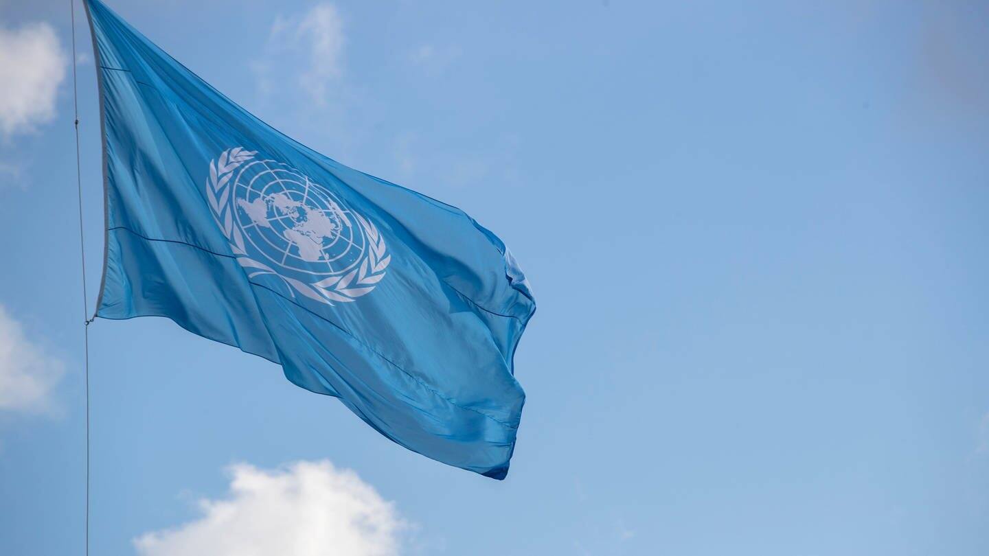 Blick auf eine Flagge der Vereinten Nationen, die vor einem blauen Himmel weht