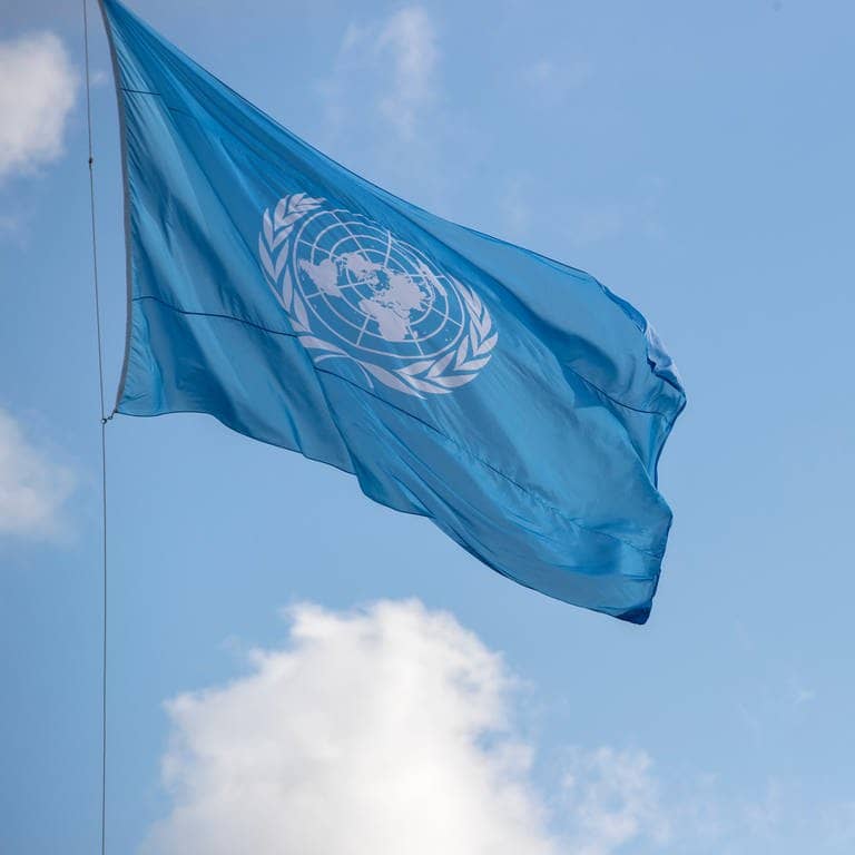 Blick auf eine Flagge der Vereinten Nationen, die vor einem blauen Himmel weht