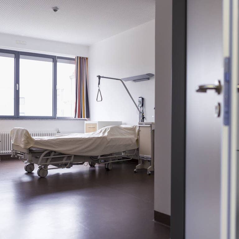 Eine Hand öffnet eine Tür zu einem leeren Bett in einem Krankenzimmer in einem Krankenhaus