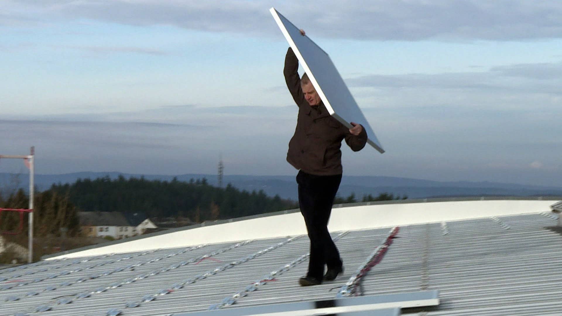 Ein Mann auf einer Photovoltaikanlage trägt eine Platte mit einem Modul für die Anlage.