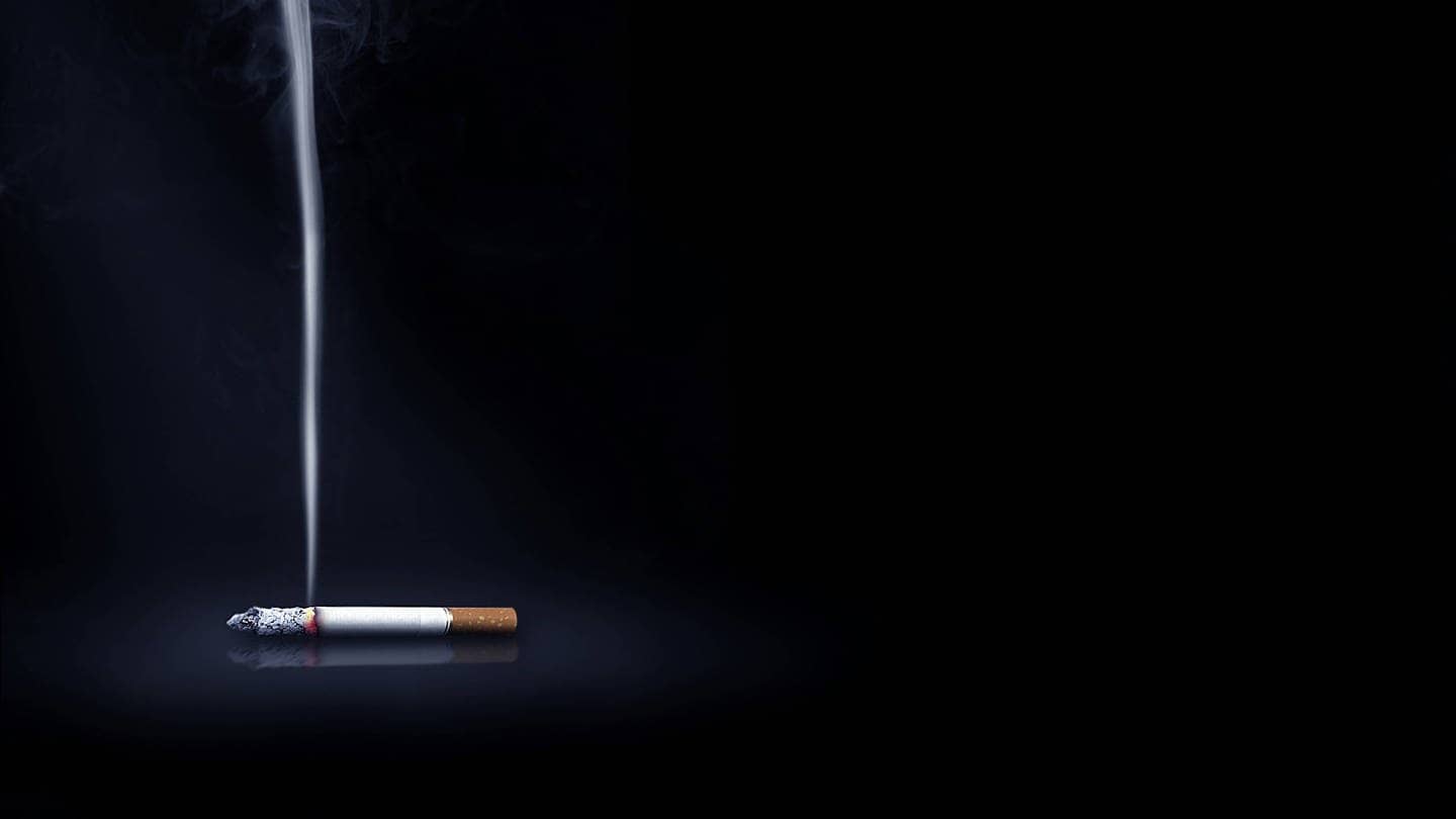 Eine qualmende Zigarette vor schwarzem Hintergrund