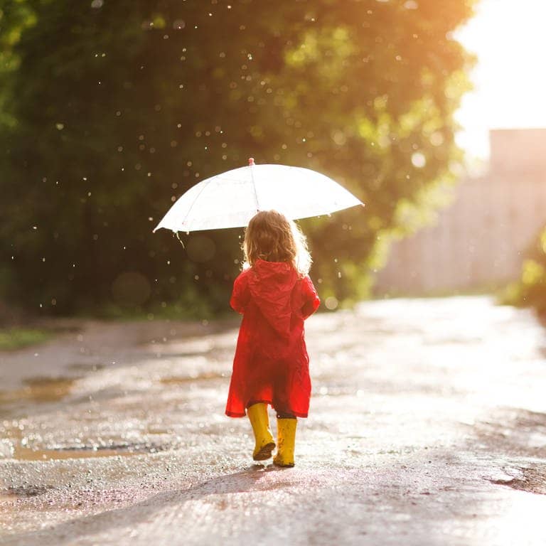 Ein Kind läuft mit Schirm und Gummistiefeln durch den Regen.