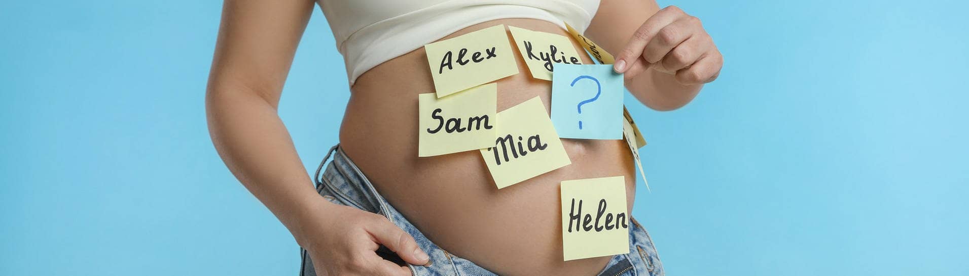 Auf den Bauch einer schwangeren Frau sind bunte Zettel mit verschiedenen Vornamen geklebt.