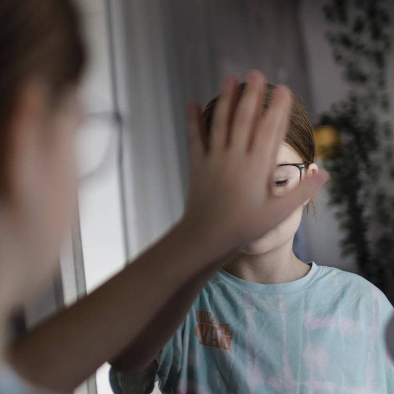 Ein Kind bedeckt sein Spiegelbild mit der Hand.