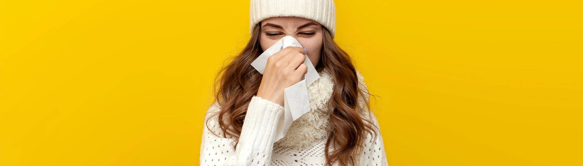 Junge Frau in Winter-Kleidung schnäuzt die Nase. Sie ist vermutlich krank und wird eine Krankschreibung für den Arbeitgeber brauchen oder sich zumindest krankmelden.
