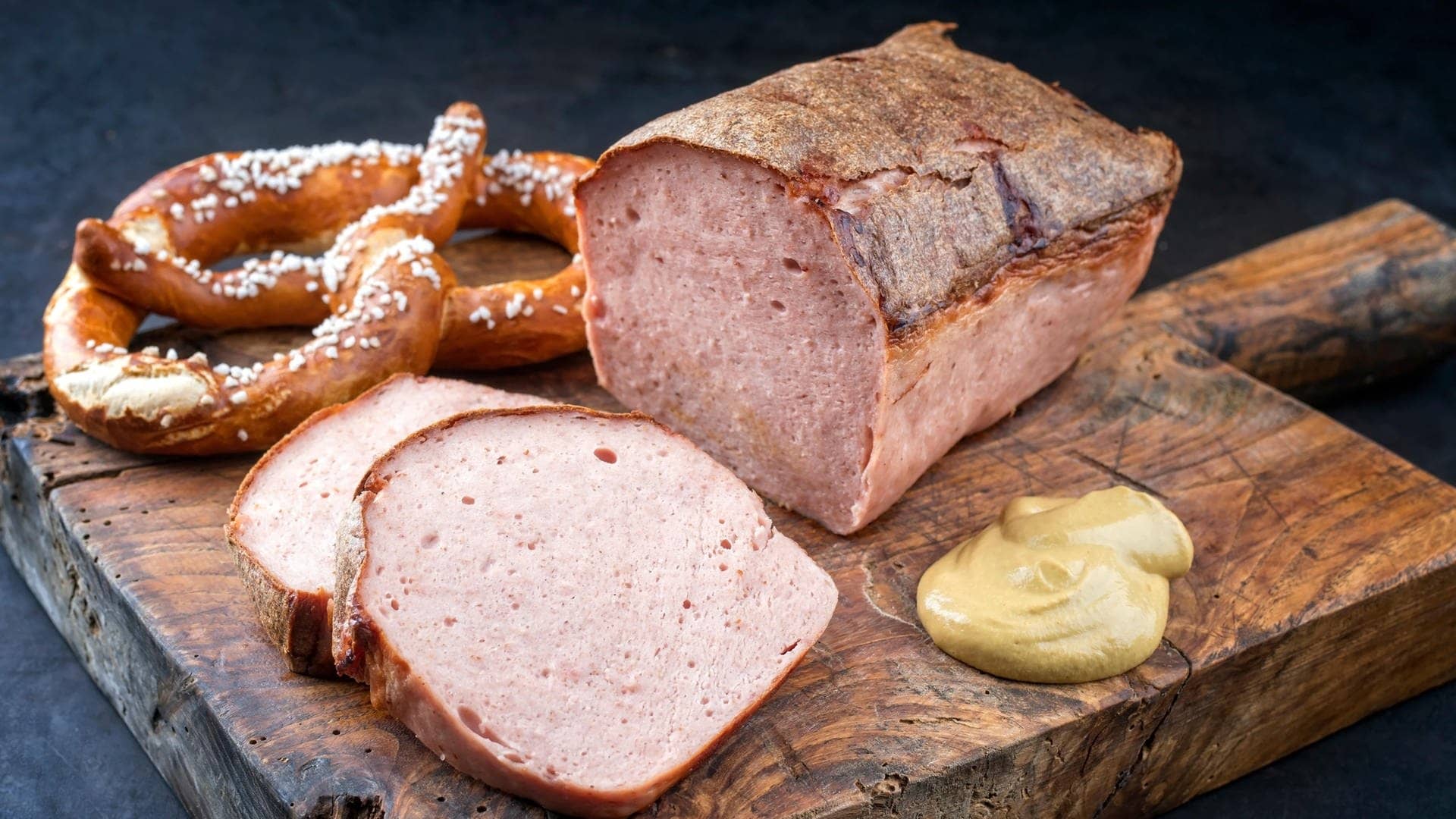Fleischkäse liebt aufgeschnitten auf einem Brett mit Senf und bayerischen Brezeln – der Begriff Fleischkäse gehört wohl in die Kategorie „widersprüchliche deutsche Wörter“. Was denn nun: Fleisch oder Käse?