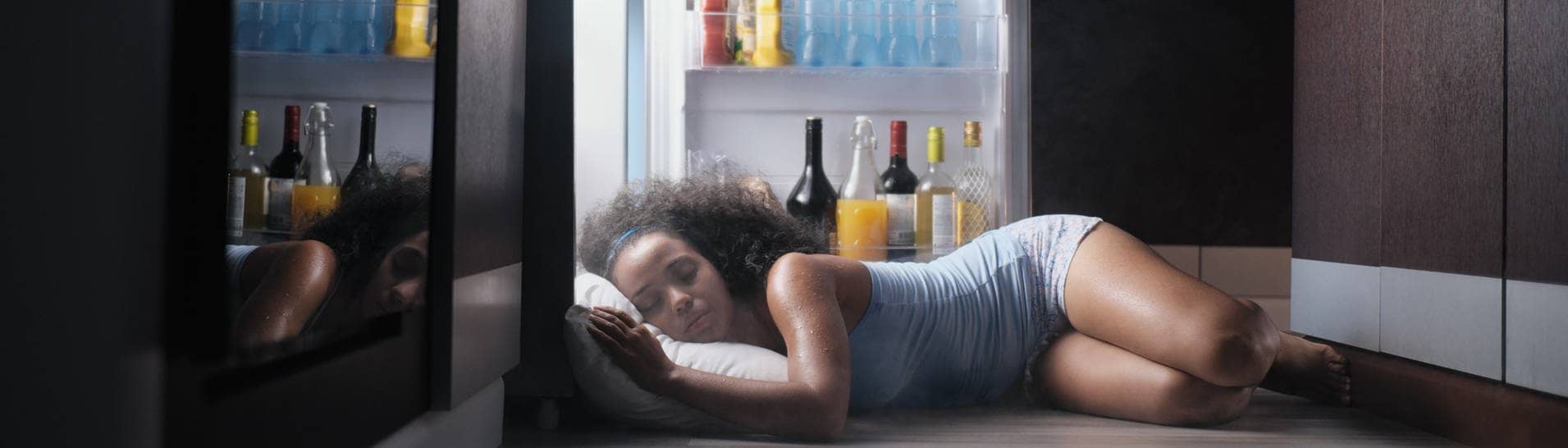 Nicht der beste Tipp: Eine Frau versucht bei der Hitze mit Kopfkissen vor dem Kühlschrank zu schlafen.
