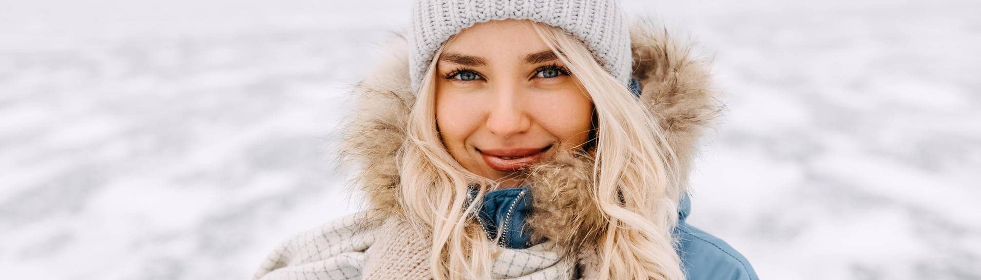 Junge Frau in Winter-Kleidung mit Mütze und Mantel steht in einer Schneelandschaft in der Kälte. Vielleicht denkt sie über Mythen rund um die kalte Jahreszeit nach.