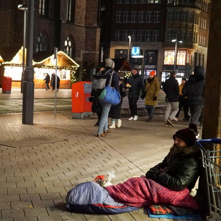Kältebusse sind im Winter überlebenswichtig für viele Obdachlose. Obdachloser sitzt auf der Straße am Weihnachtsmarkt.