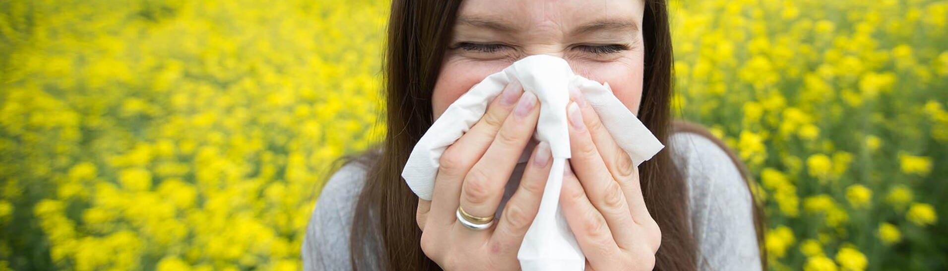 Pollen sind lästig – junge Frau mit Allergie putzt sich die Nase