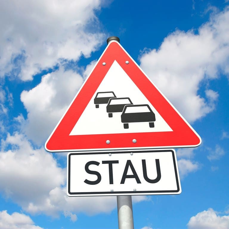 Straßenschild vor blauem Himmel mit Autos, das auf einen Stau im Verkehr hinweist (Foto: Adobe Stock, bluedesign)