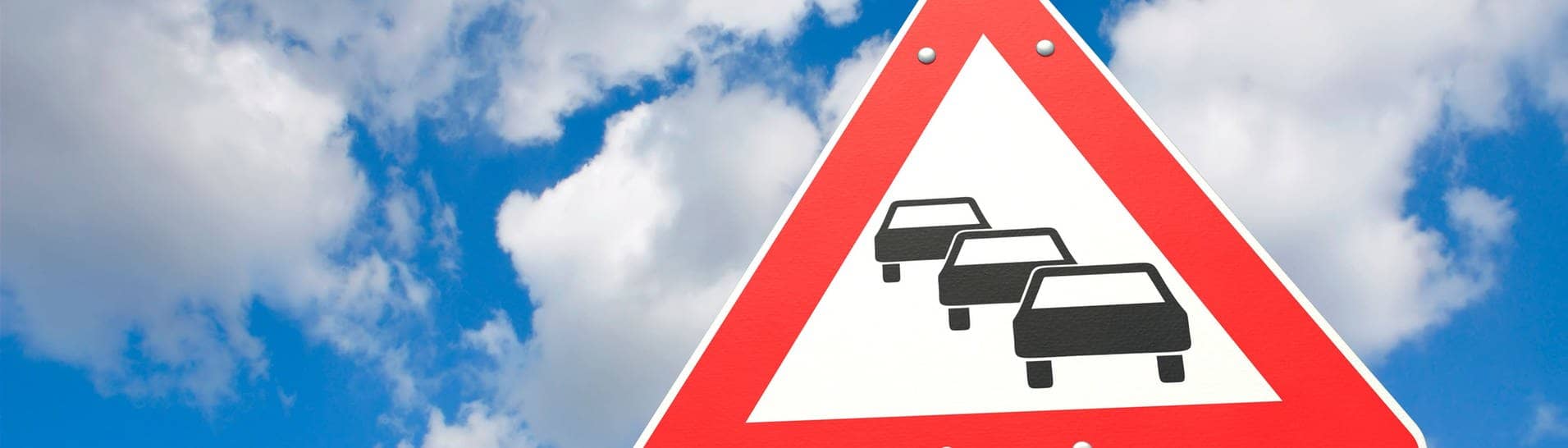Straßenschild vor blauem Himmel mit Autos, das auf einen Stau im Verkehr hinweist