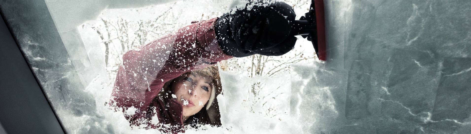 Junge Frau mit Enteiser, sie kratzt die verschneite und gefrorene Scheibe des Autos im Winter frei. (Foto: IMAGO, IMAGO / Westend61)