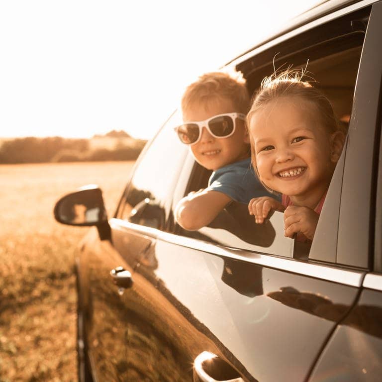Ein Junge mit Sonnenbrille und ein Mädchen schauen aus dem Fenster eines Autos und lachen