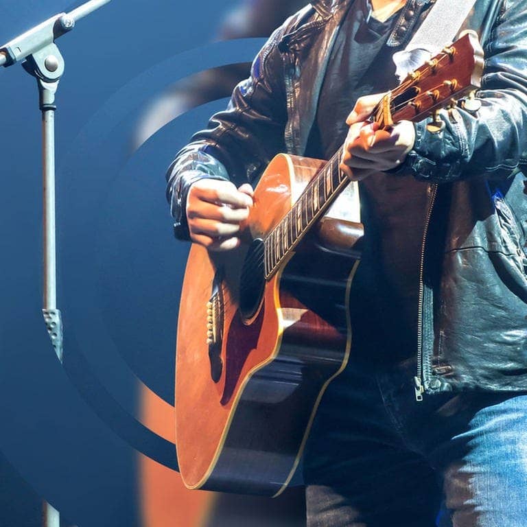 Ein Musiker spielt bei einem Auftritt auf einer Akustik-Gitarre (Foto: Adobe Stock, v74)