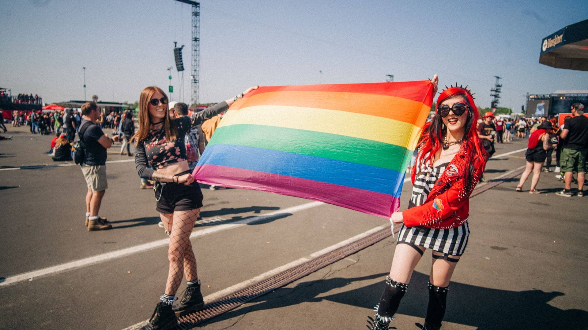 Zwei junge Frauen laufen auf dem Gelände von Rock am Ring herum und tragen zwischen sich eine Regenbogenflagge
