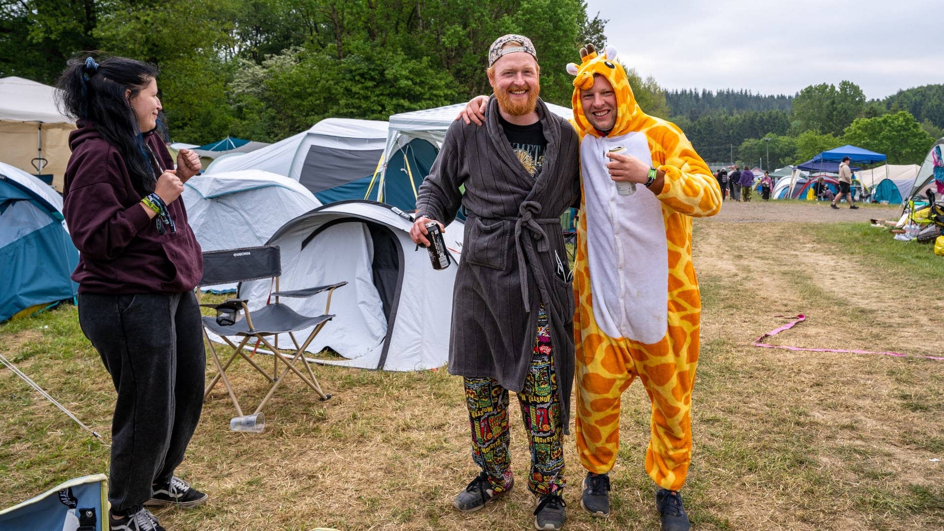 Zwei junge Männer und eine Frau sind auf dem Campingplatz bei Rock am Ring bereits morgens gut gelaunt mit Giraffen-Kostüm und Bademantel bekleidet