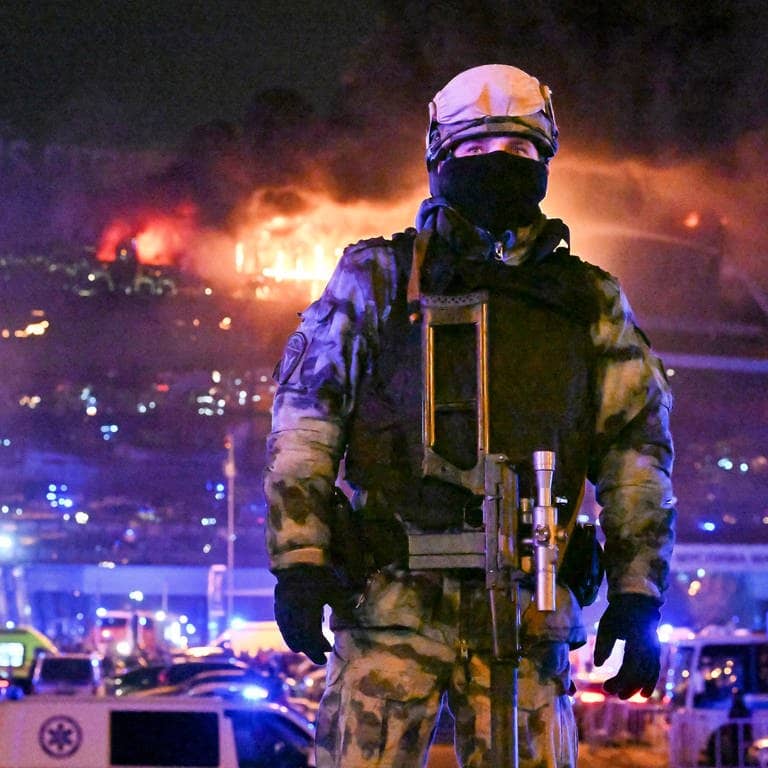 Ein Soldat der russischen Nationalgarde (Rosgwardija) sichert ein Gebiet, während über Crocus City Hall am westlichen Rand Moskaus ein gewaltiger Brand zu sehen ist. 