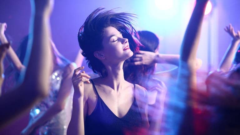 Junge F rau in Kleid tanzt mit geschlossenen Augen im Scheinwerferlicht auf einer Party