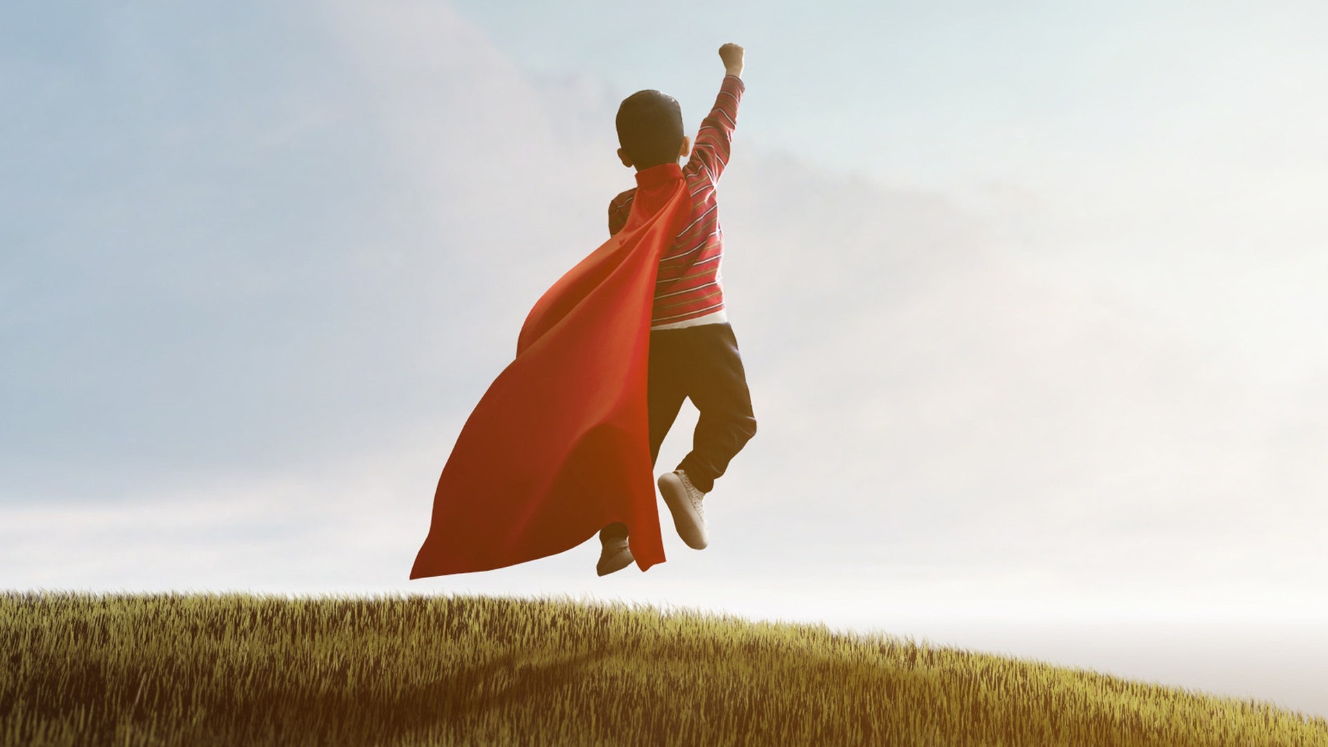 Junge mit Superhelden-Cape auf einer Wiese von hinten. (Foto: Adobe Stock, Jess rodriguez)