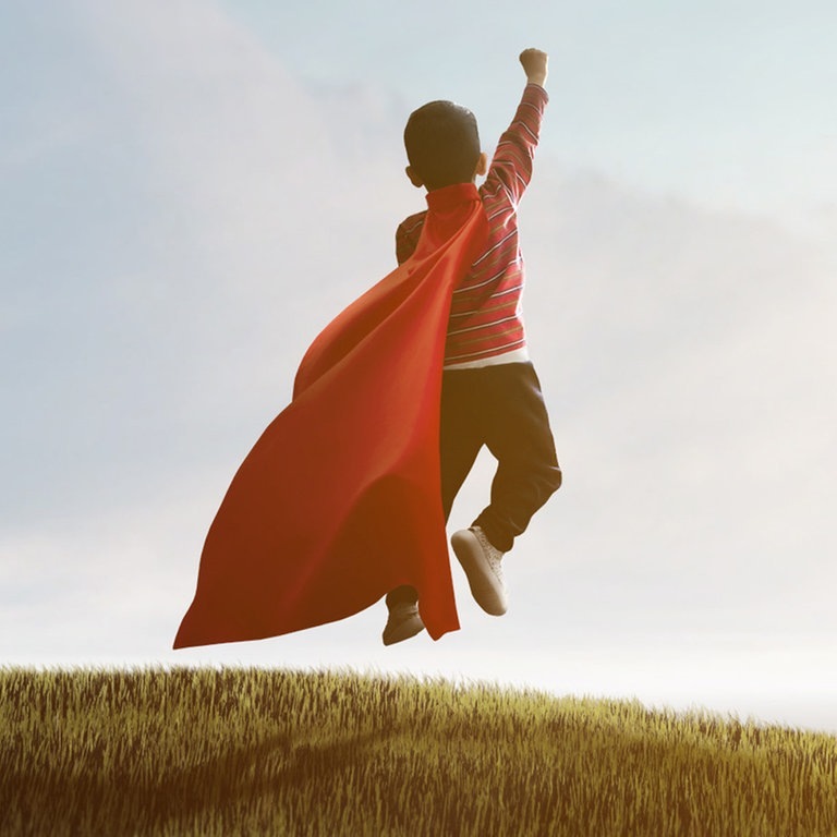 Junge mit Superhelden-Cape auf einer Wiese von hinten. (Foto: Adobe Stock, Jess rodriguez)
