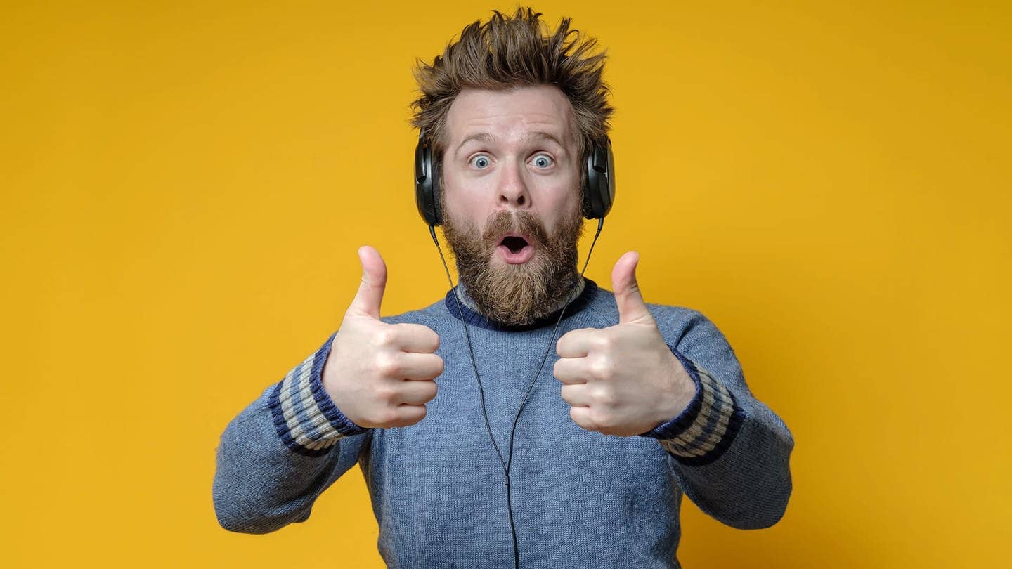 Ein freudig überraschter Mann mit Kopfhörern hört Musik und macht eine anerkennende Geste, den Daumen hoch. Gelber Hintergrund. (Foto: Adobe Stock, koldunova)