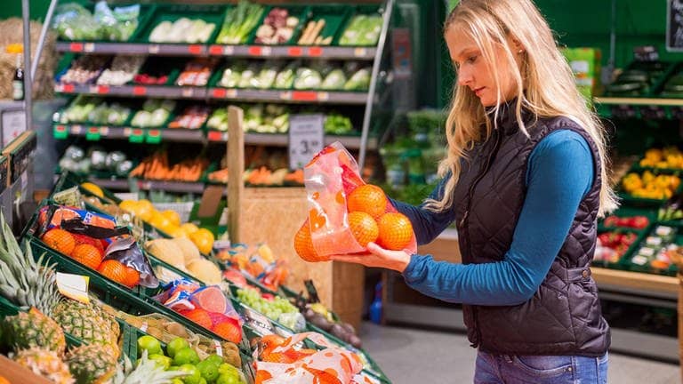 Eine Frau vergleicht in einem Supermarkt ein Netz Orangen (Foto: dpa/picture-alliance.de/Benjamin Nolte)