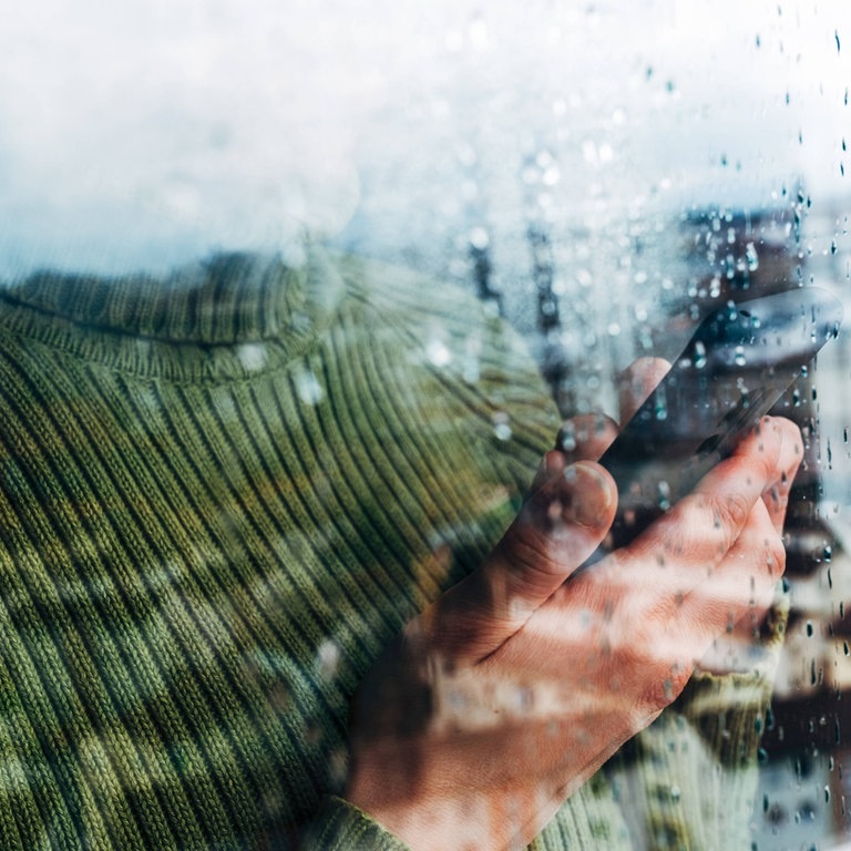 Frau im grünen Pullover hält Telefon in der Hand (Foto: IMAGO, Addictive Stock)