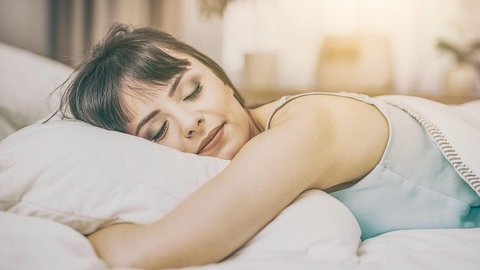 Eine Frau liegt gemütlich auf ihrem Kopfkissen im Bett (Foto: Adobe Stock/REDPIXEL)