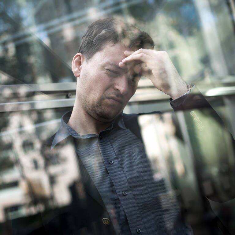 Mann mit Kopfschmerzen und hand an der Stirn spiegelt sich in einer Glasscheibe (Foto: picture-alliance / Reportdienste, picture alliance / dpa Themendienst | Alexander Heinl)