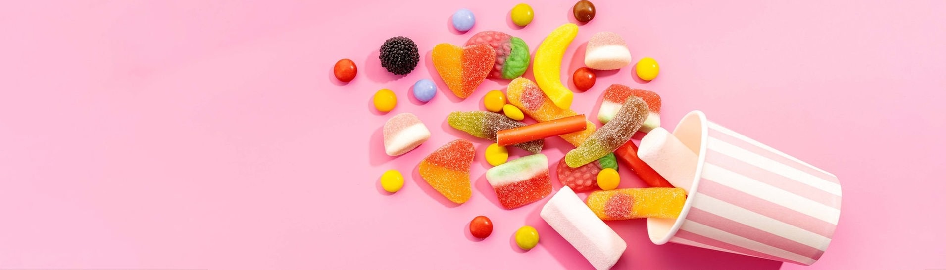 Bunte Fruchtgummis fallen aus einem gestreiften Papierbecher (Foto: IMAGO, Addictive Stock)