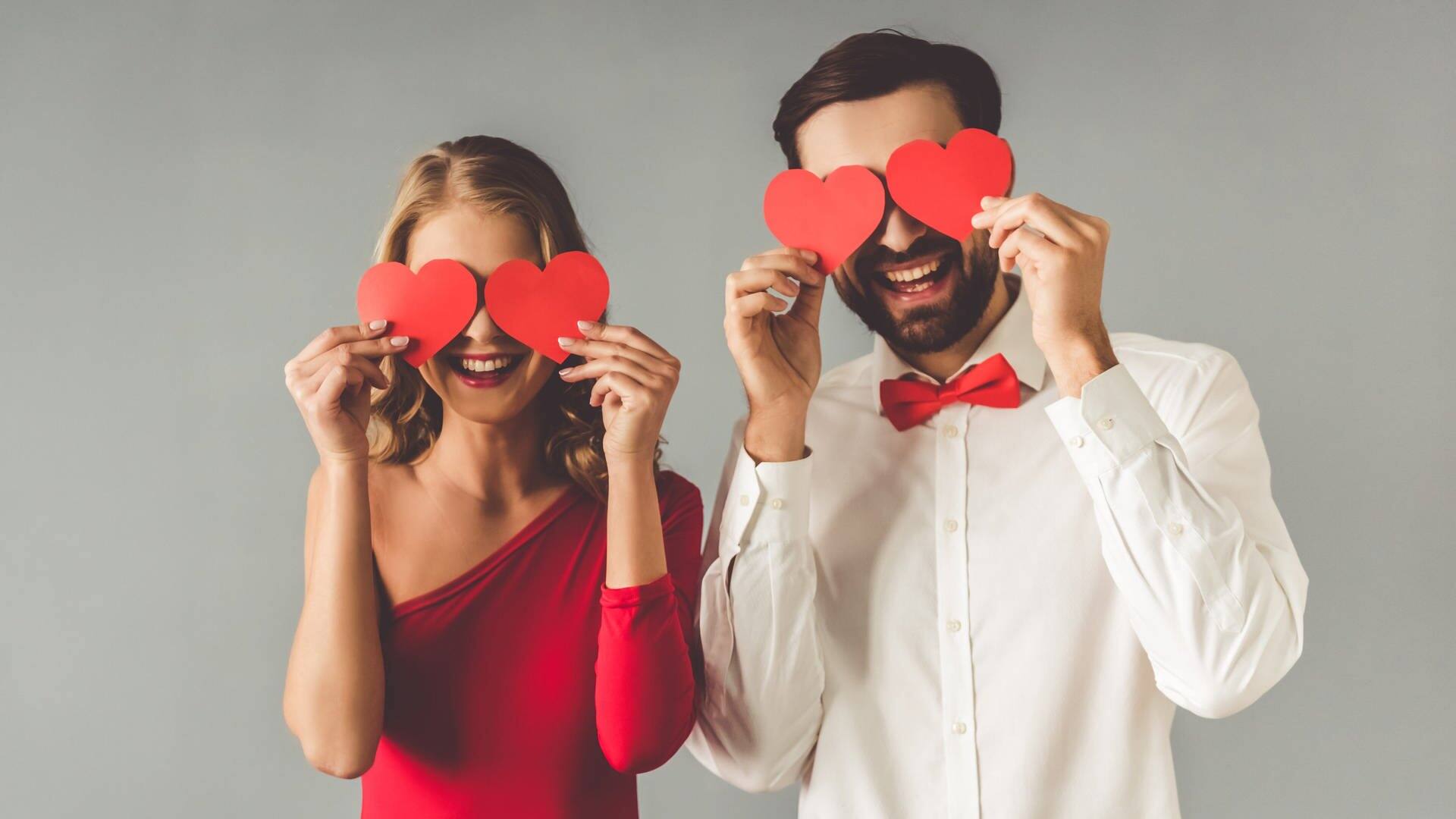 Ein Mann und eine Frau halten sich rote Papierherzen vor die Augen. Zweisamkeit gehört zu den fünf Sprachen der Liebe in Beziehungen. (Foto: IMAGO, agefotostock)