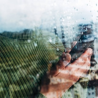 Frau im grünen Pullover hält Telefon in der Hand