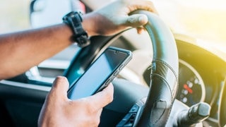 Mann hält Telefon am Steuer in der Hand