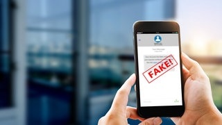 Person hält Smartphone in der Hand auf der eine SMS abgebildet ist, ein roter Fake-Banner ist darüber